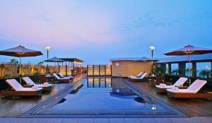 a pool with chairs and umbrellas on a deck at Grand Mercure Agra - An Accor Brand in Agra