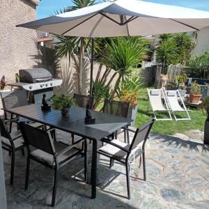 une table et des chaises noires avec un parasol et un grill dans l'établissement Maison bord de mer, à Penta-di-Casinca