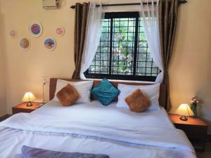 een slaapkamer met een wit bed met kussens en een raam bij Quirky Stays -2bhk house with terrace in Candolim