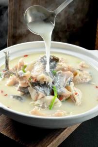 a spoon of milk being poured onto a bowl of seafood soup at Yosemite Riverview Homestay in Yichang