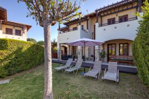 a group of chairs and an umbrella in front of a house at 2 bedroom Apartment Kalypso with private garden, Aphrodite Hills Resort in Kouklia