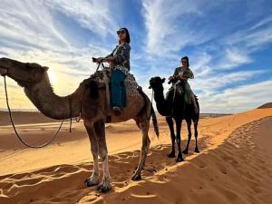 two women riding on camels in the desert at Global Luxury Camp in Merzouga