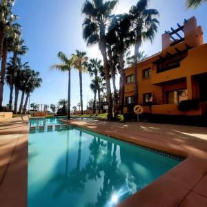 a swimming pool with palm trees in front of a building at Casa Allegra in Los Alcázares