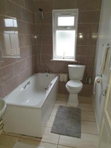 ein Bad mit einer Badewanne, einem WC und einem Fenster in der Unterkunft SAV Apartments Watford in Watford