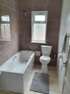 baño con bañera, aseo y ventana en SAV Apartments Watford, en Watford