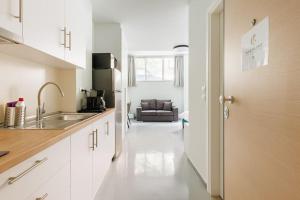 Snug studio apartment with shared garden IV في أثينا: مطبخ بدولاب بيضاء ومغسلة وأريكة
