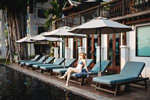 una mujer sentada en una silla junto a una piscina en Buri Sriping Riverside Resort & Spa - SHA Extra Plus, en Chiang Mai