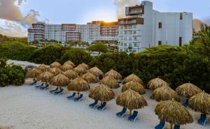 Embassy Suites By Hilton Aruba Resort في شاطئ بالم إيغل: مجموعة من مظلات القش والكراسي على الشاطئ
