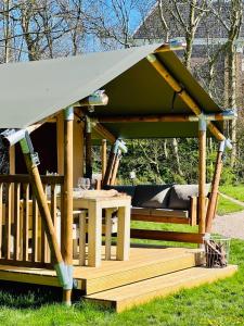 a wooden gazebo with a table in the grass at Camping Zee van Tijd Holwerd in Holwerd