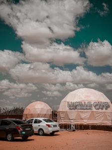Rum Lucille Luxury camp في وادي رم: خيمتان مع سيارات متوقفة في حقل ترابي