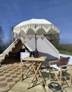 einen Tisch mit einem Sonnenschirm und zwei Stühlen vor einem Zelt in der Unterkunft Luxury Tent with Restroom and shower, close to the Beach in Ystad