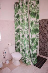 a bathroom with a toilet and a green leafy shower curtain at Escape House in Tarrafal