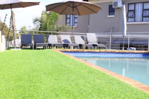 a swimming pool with chairs and an umbrella and grass at ANGELOCEAN GUEST HOUSE in Witbank