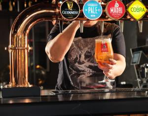 a man holding a glass of beer behind a bar at Radisson RED London Gatwick Airport in Crawley