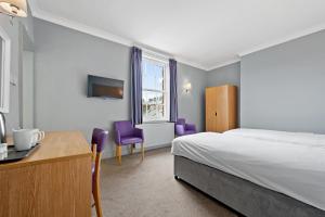 1 dormitorio con cama, escritorio y sillas moradas en The Royal Hotel Whitby en Whitby