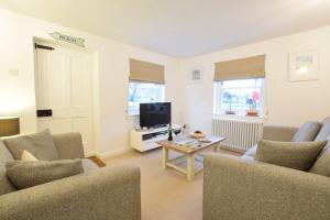 a living room with chairs and a tv and a table at 1 South Cottages in Thorpeness