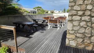 una terraza con mesas y bancos de madera y una pared de piedra. en Stonehouse on Main, en Struisbaai