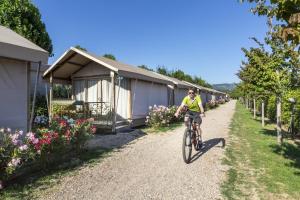 a man riding a bike down a gravel road next to tents at hu Venezia Camping in Town in Marghera