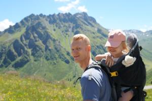 a man holding a child in a backpack on a mountain at Sporthotel Bachmann in Gargellen