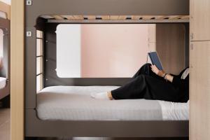 Local Hostel & Suites في مدينة كورفو: شخص يستلقي على سرير بطابقين يقراء كتاب