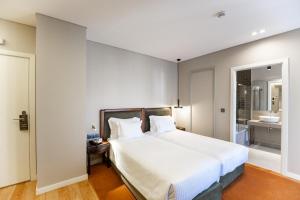 a bedroom with a large white bed and a bathroom at Avenida Boutique Hotel in Viseu