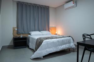 a bedroom with a bed with white sheets and a window at DICOPI HOTEL in Maringá