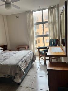 een slaapkamer met een bed, een bureau en een raam bij Beach Bliss in Amanzimtoti