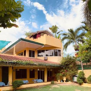 a yellow house with chairs and palm trees at Abihon HoferHaus Mactan Guesthouse in Lapu Lapu City