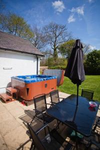 a patio with a table and an umbrella and a hot tub at Glyncoch Isaf Llangrannog in Llangranog