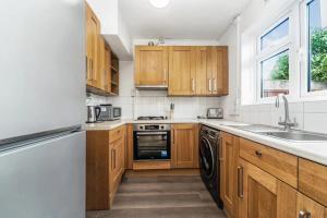 cocina con armarios de madera, fregadero y lavavajillas en Pass the Keys Spacious Family Home in London, en Londres