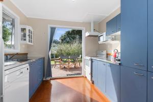 a kitchen with blue cabinets and a view of a patio at Teal Bay Treasure - Teal Bay Holiday Home in Whangaruru North