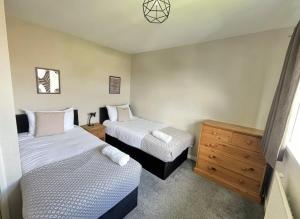 a bedroom with two beds and a wooden dresser at Contractors welcome 3 bed house with parking by Eagle Owl Stays in Crawley