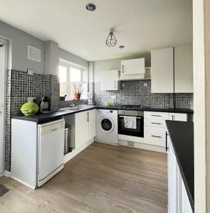 a kitchen with white cabinets and a washer and dryer at Contractors welcome 3 bed house with parking by Eagle Owl Stays in Crawley