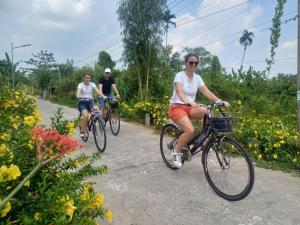 three people riding bikes down a path with flowers at AUTHENTIC HOMESTAY in Can Tho