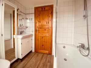 ein Badezimmer mit einer Holztür, einer Badewanne und einem Waschbecken in der Unterkunft Damm-Kate in Zingst