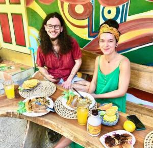 Um homem e uma mulher sentados à mesa com comida. em Real Jamaica - Cabin right beside the sea-Papa Curvins Yard em Oracabessa