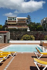 a swimming pool with chairs and a building in the background at Lovely Apartment in San Agustín: Steps Away from Playa Del Inglés and Maspalomas! in San Bartolomé de Tirajana