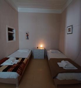 Amaryllis Guest House في هيدرا: سريرين في غرفة صغيرة مع ضوء على طاولة