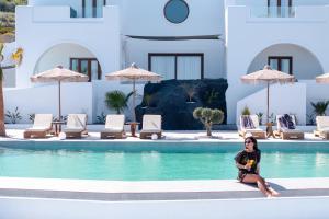 een vrouw die naast een zwembad zit bij Leon Luxury Suites in Imerovígli