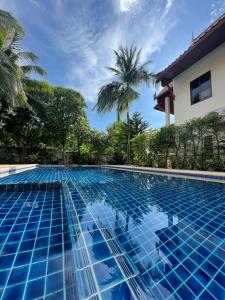 a blue swimming pool with palm trees in the background at Aisawan Resort villa in Surin Beach