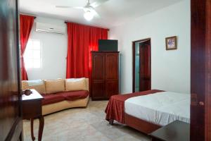 1 dormitorio con cama, sofá y cortinas rojas en Hotel Nuevo Amanecer, en El Catey