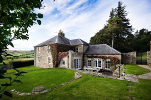 une ancienne maison en pierre avec une pelouse verte dans l'établissement Broadgate House & Steading, à West Woodburn