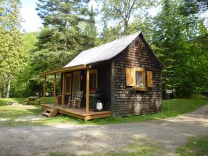 Cette petite cabane en rondins dispose d'une terrasse couverte et d'une chaise. dans l'établissement Rivière Petit Saguenay, à Petit-Saguenay