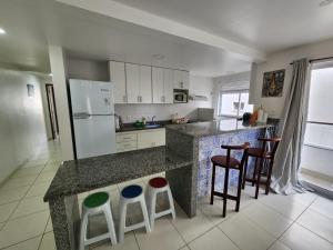cocina con encimera con taburetes y nevera en Quadra mar- Apto 2 quartos com ar!, en Arraial do Cabo