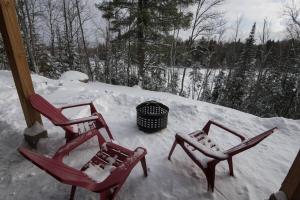 2 chaises rouges assises dans la neige sur une terrasse couverte dans l'établissement Panoramic Lakefront Chalet with Hot Tub & Firepit, à Chertsey