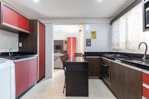 une grande cuisine avec des plans de travail noirs et des touches de rouge dans l'établissement Apartamento em Bombas - Ótimo para Famílias, à Bombinhas