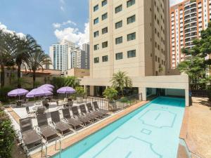 a swimming pool with chairs and umbrellas in front of a building at Hotel M Privilege Moema São Paulo in Sao Paulo