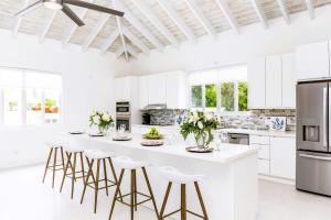 a white kitchen with a large white island with stools at Caribbean Escape Luxe Waterfront Villa with Pool in Long Bay Hills