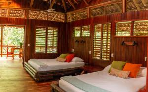 2 camas en una habitación con paredes y ventanas de madera en Encanta La Vida, en Cabo Matapalo