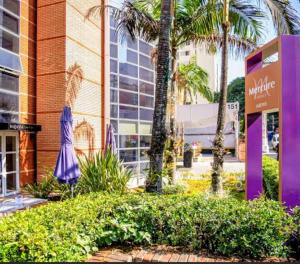 聖保羅的住宿－Hotel M-RCURE Av Paulista GRAND PLAZA - Master Deluxe king Studio Veranda - Executive Class - By LuXXoR，一座棕榈树和紫色标志的建筑
